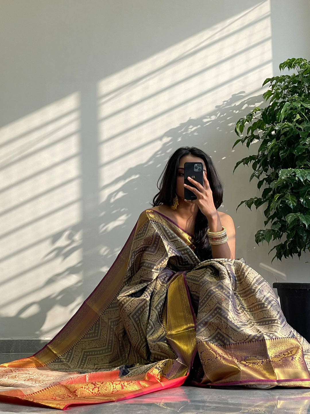 Model seated, displaying gold zari Kanjivaaram silk saree.