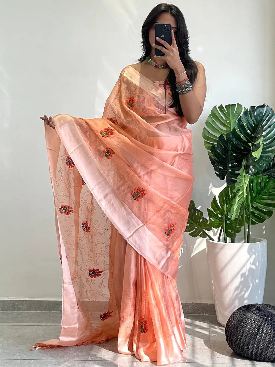 Model wearing chiffon satin saree with floral design, holding phone.