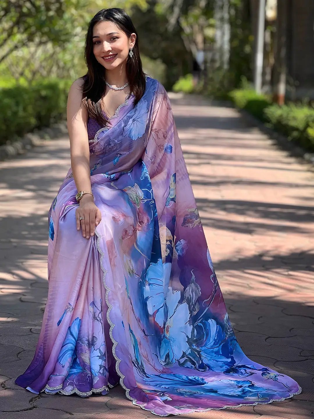 Model seated wearing lavender floral print saree, outdoor setting.