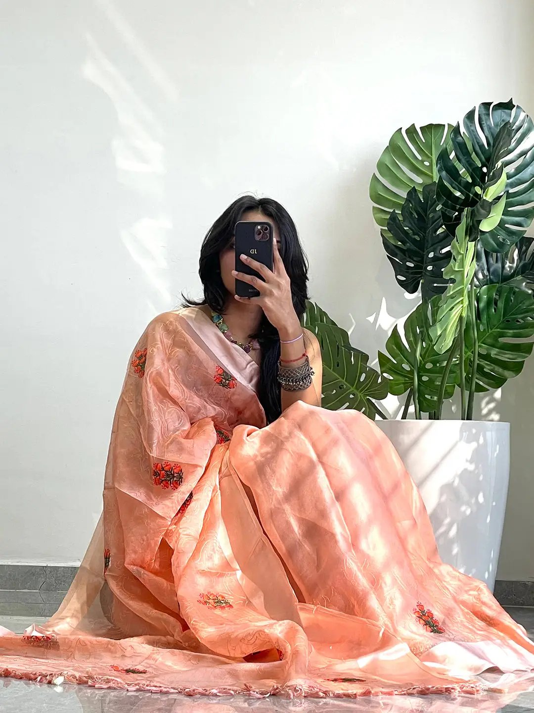 Seated model in chiffon satin saree with floral embroidery.