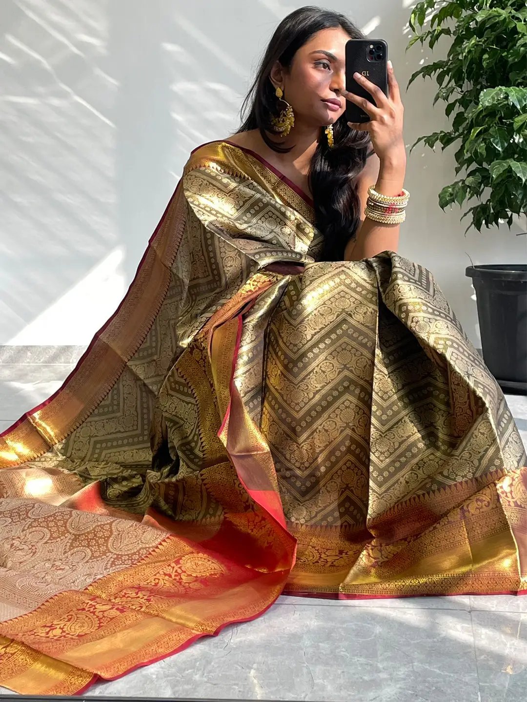 Seated model in gold zari Kanjivaaram pattu silk saree, holding phone.