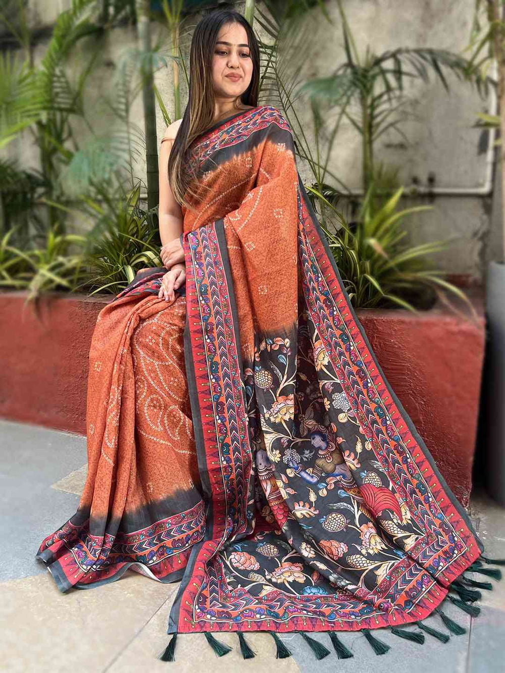 Seated model in orange saree with Bandhej and Kalamkari details