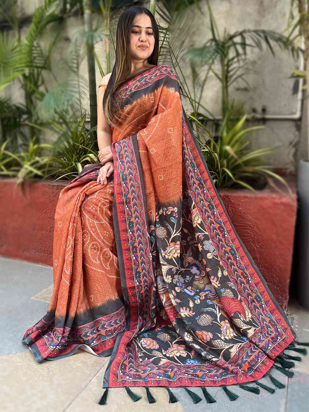 Seated model in orange saree with Bandhej and Kalamkari details