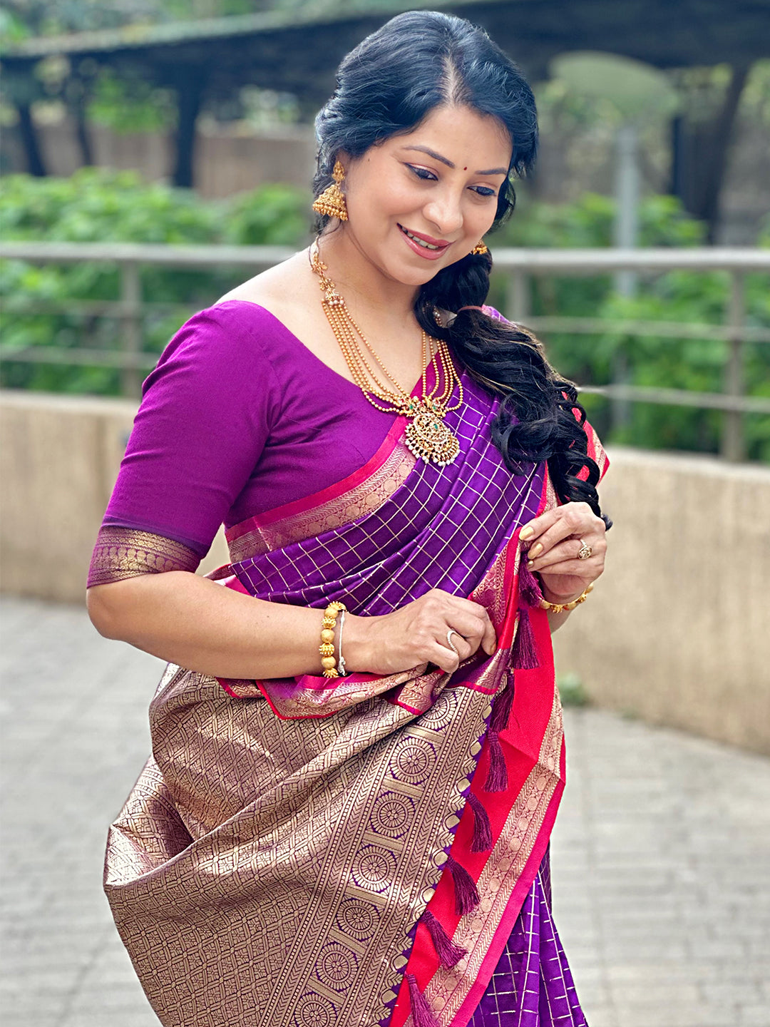 Woman adjusting purple silk saree with intricate gold design.