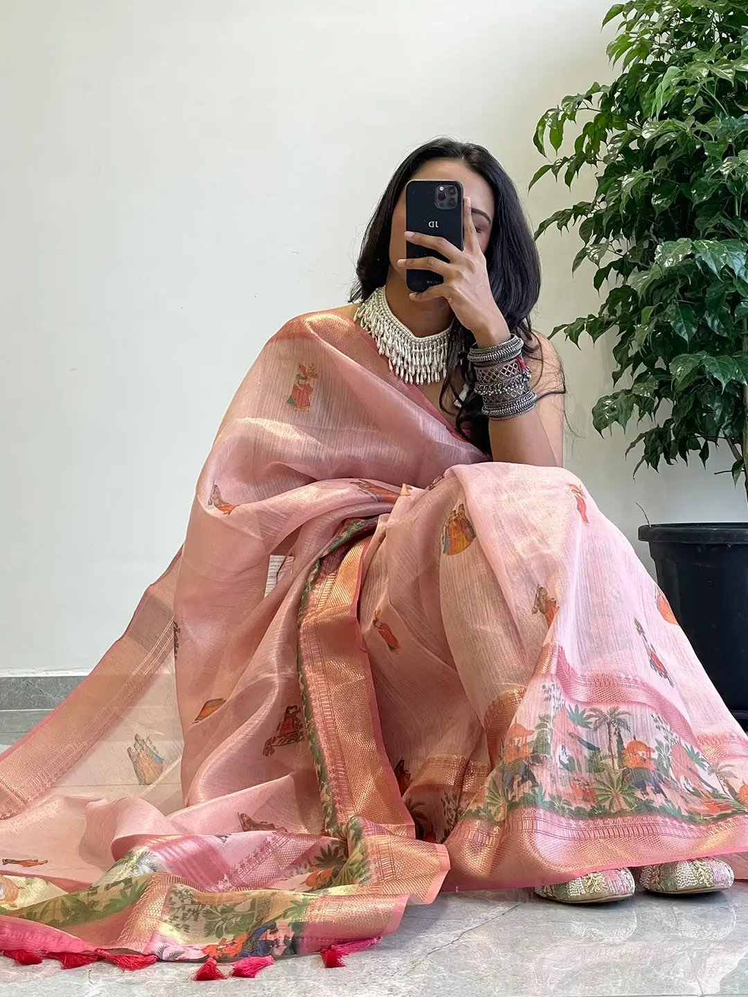 Model sitting in soft gold zari tissue saree with intricate digital print.