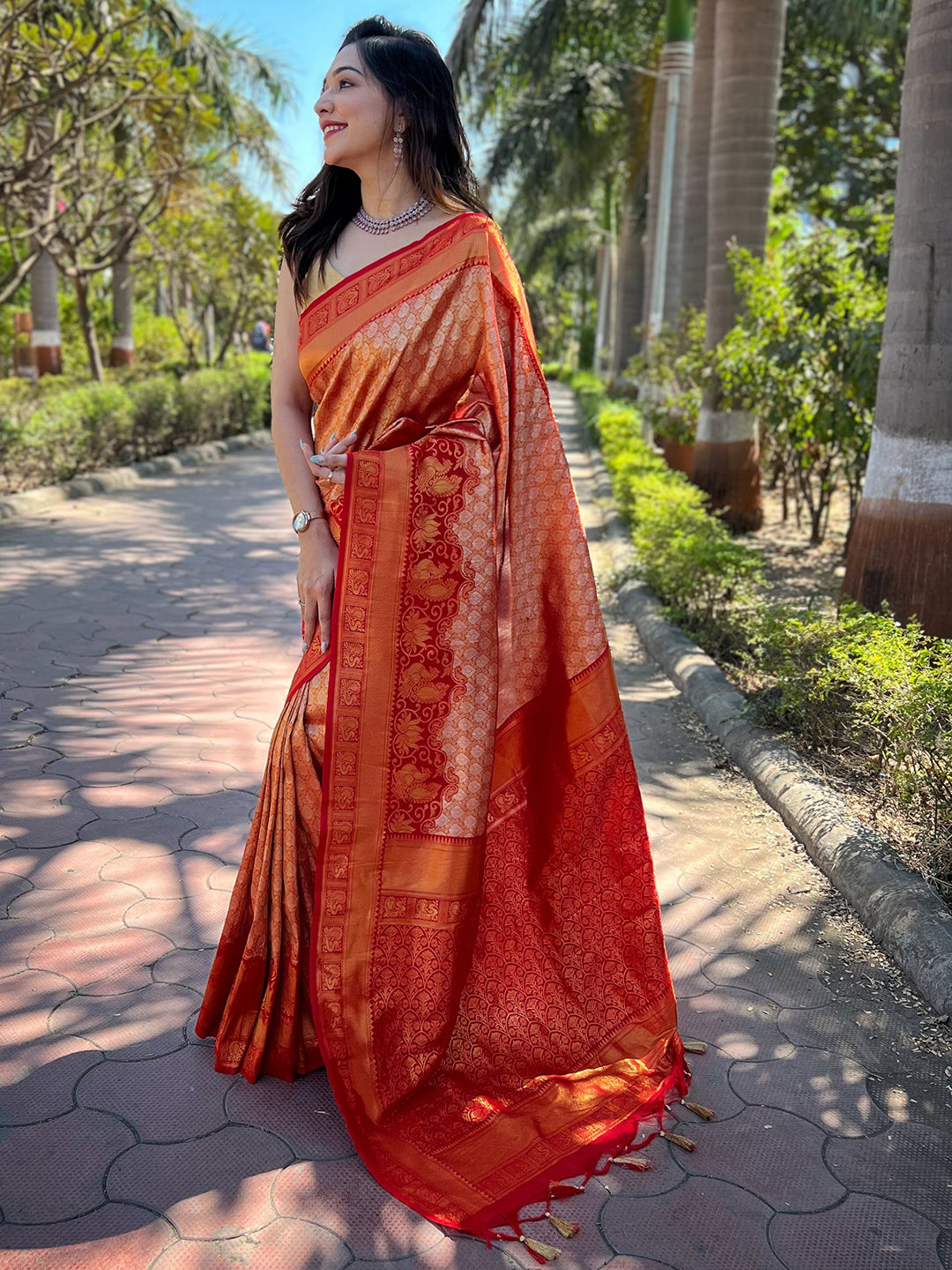 Model wearing orange-red Kanjivaram saree with intricate patterns