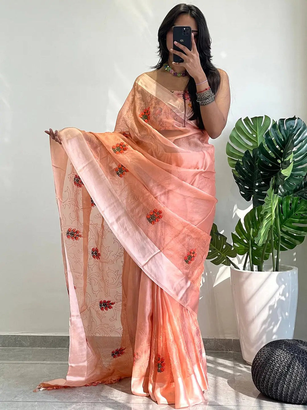Model wearing chiffon satin saree with floral design, holding phone.