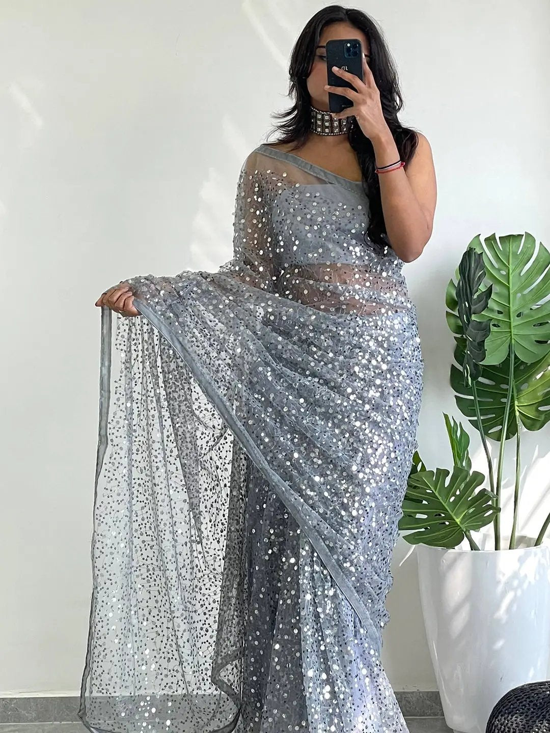 Woman in a net saree adorned with sequins, holding a phone.