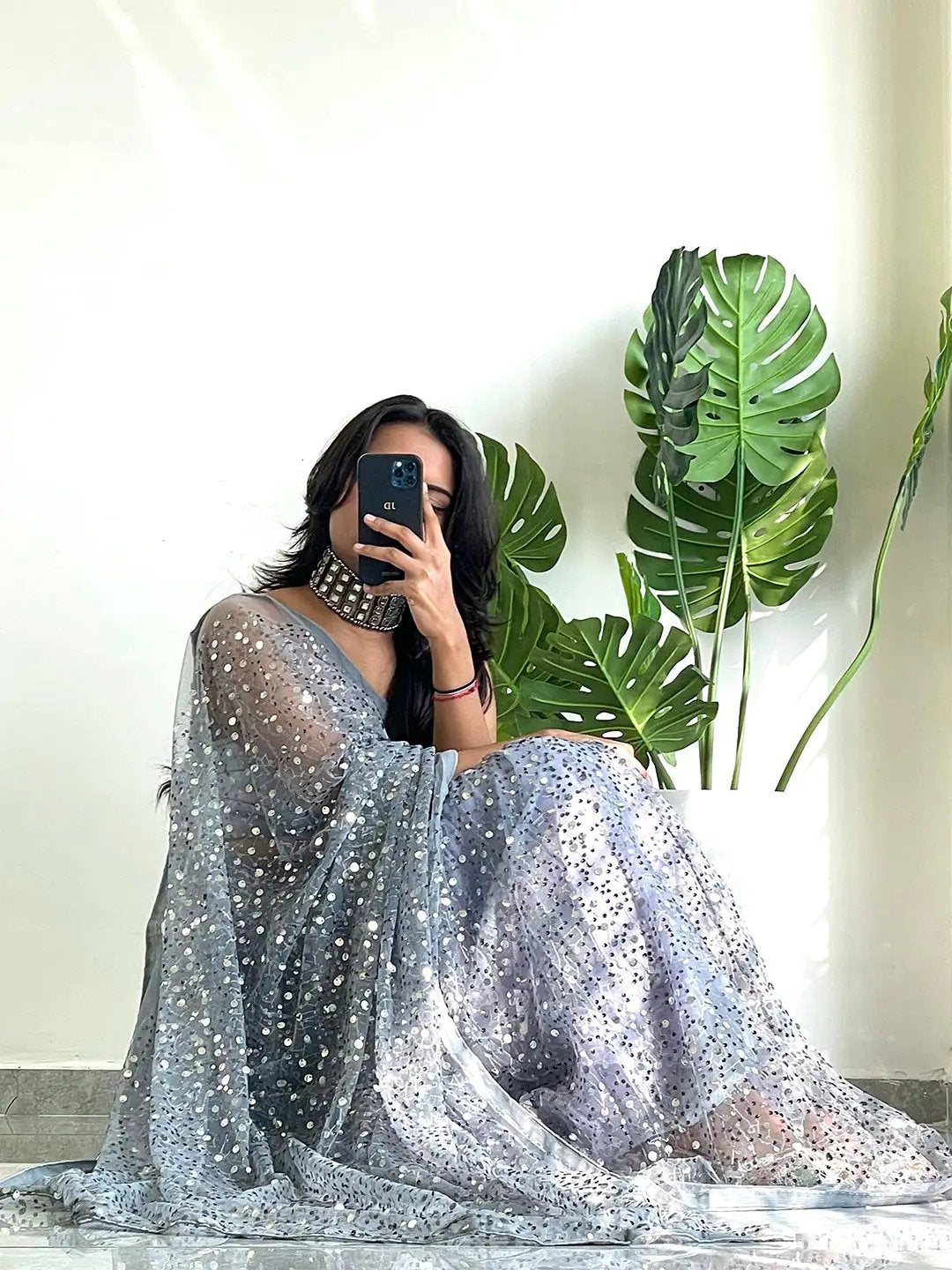 Sitting pose of a model in a sequined net saree, taking a selfie.