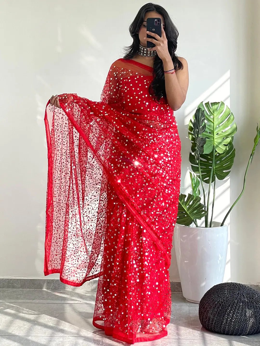 Model taking mirror selfie in red net saree with sequins.
