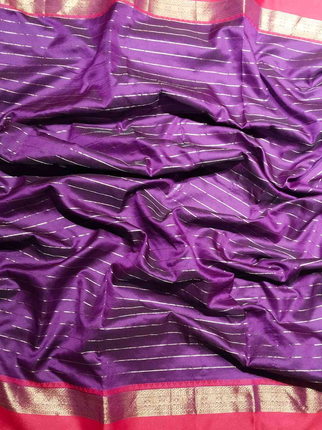 Close-up of purple silk saree fabric with red and gold border.