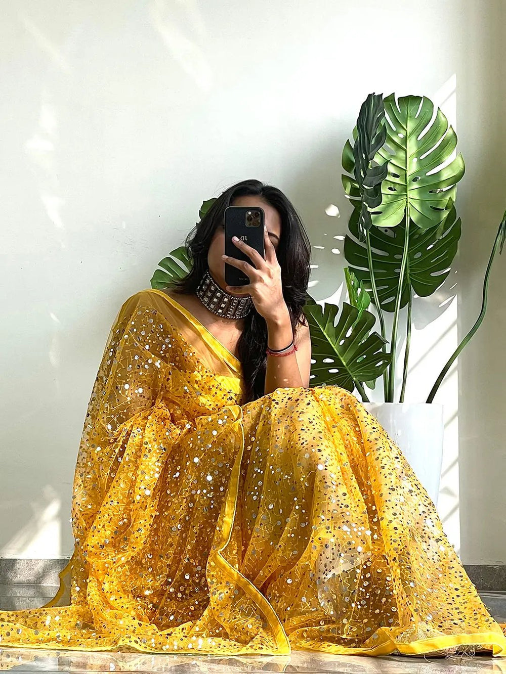 Sitting model in yellow sequined net saree, holding phone