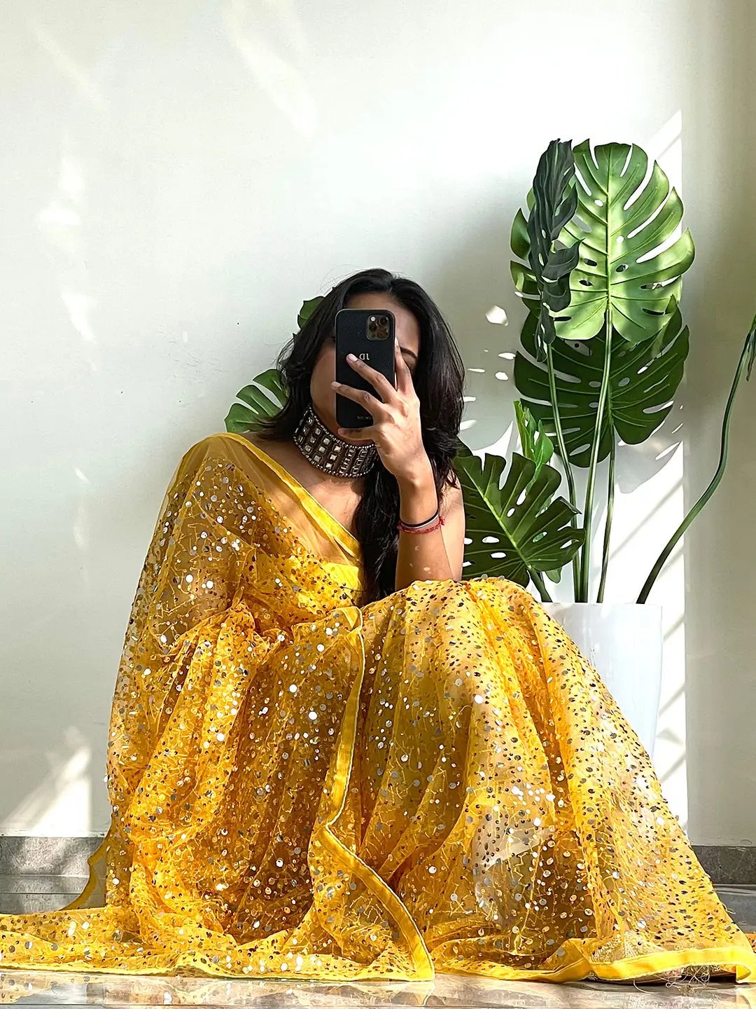 Sitting model in yellow sequined net saree, holding phone