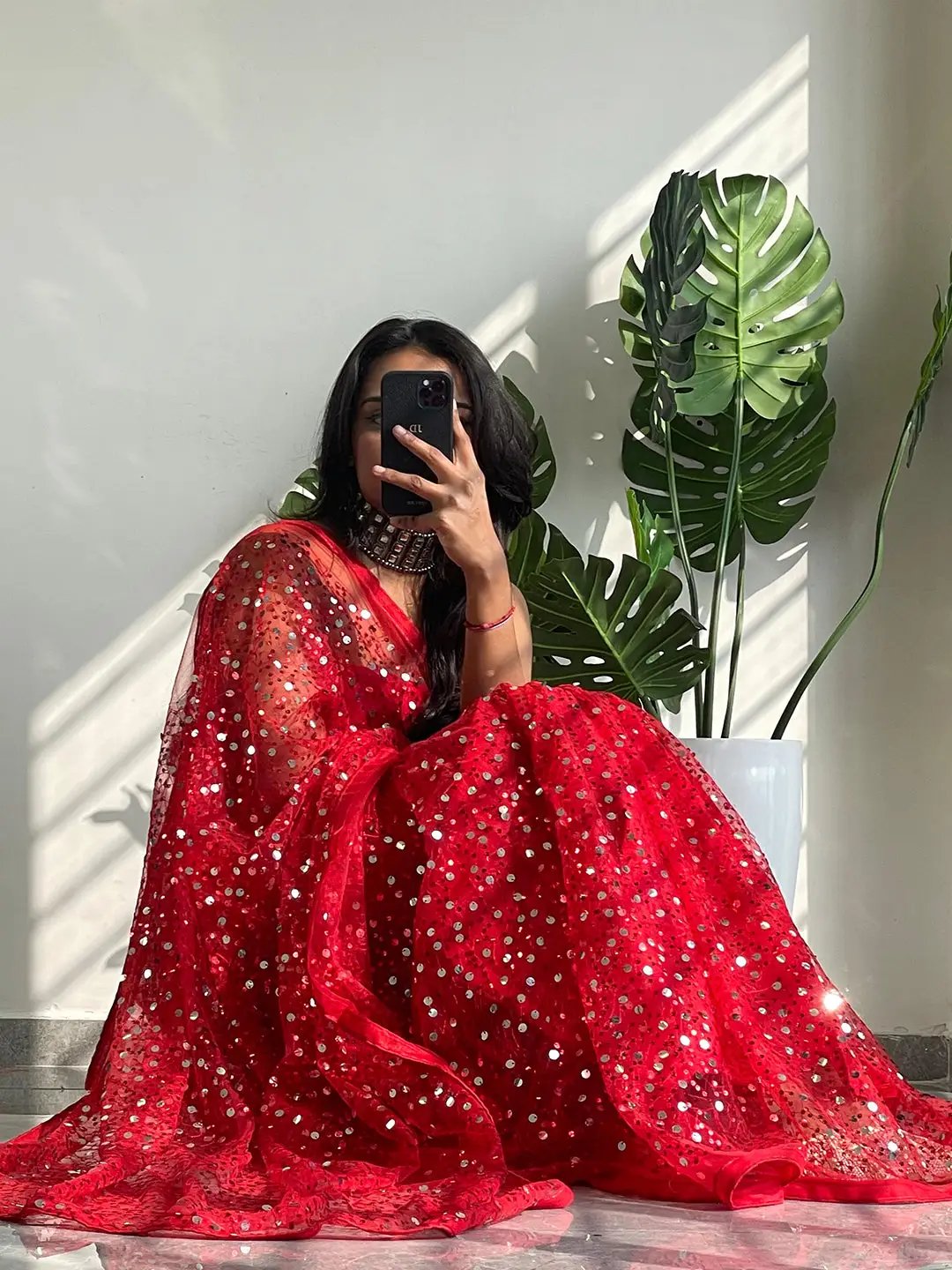 Model sitting in red net saree with sequins embroidery.