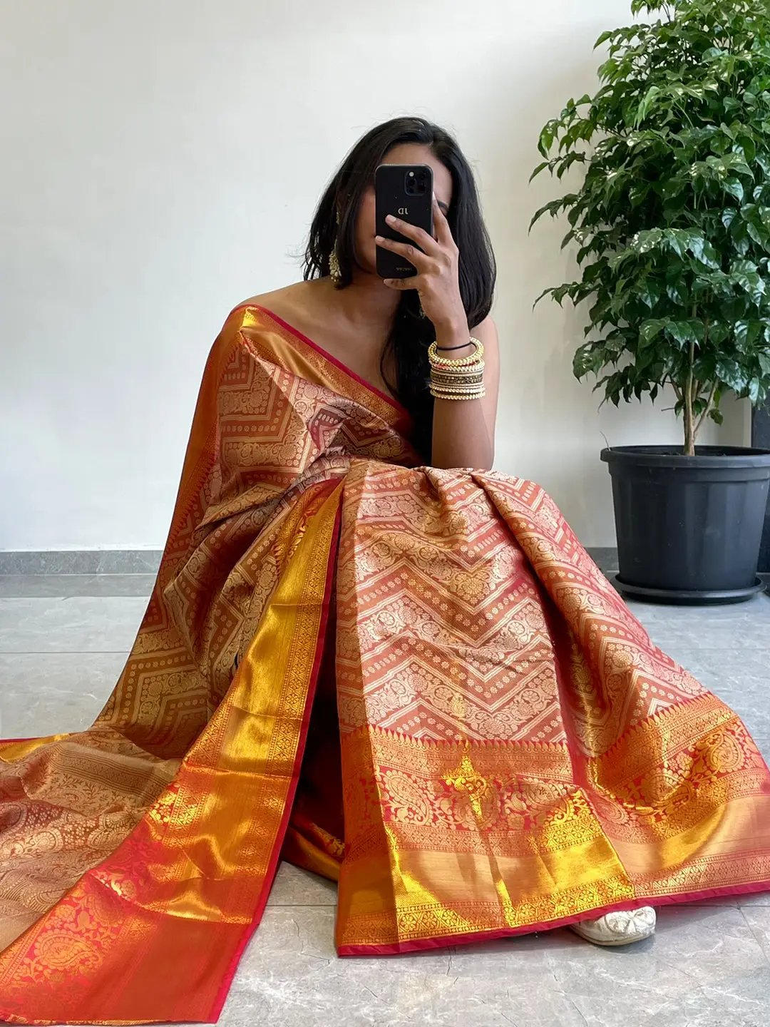 Seated model in gold zari Kanjivaaram silk saree, holding phone.