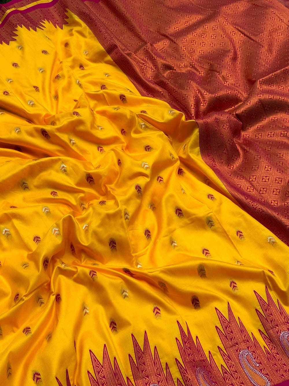 Yellow silk saree with detailed border and embroidery spread on grass
