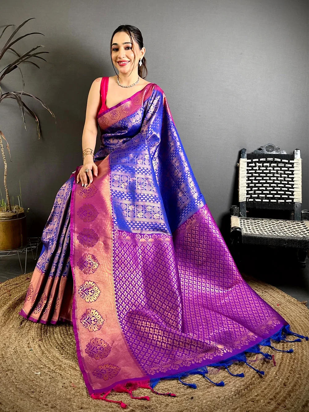 Royal blue soft silk zari woven saree, seated model with the magenta zari pallu and tassels spread on a jute rug