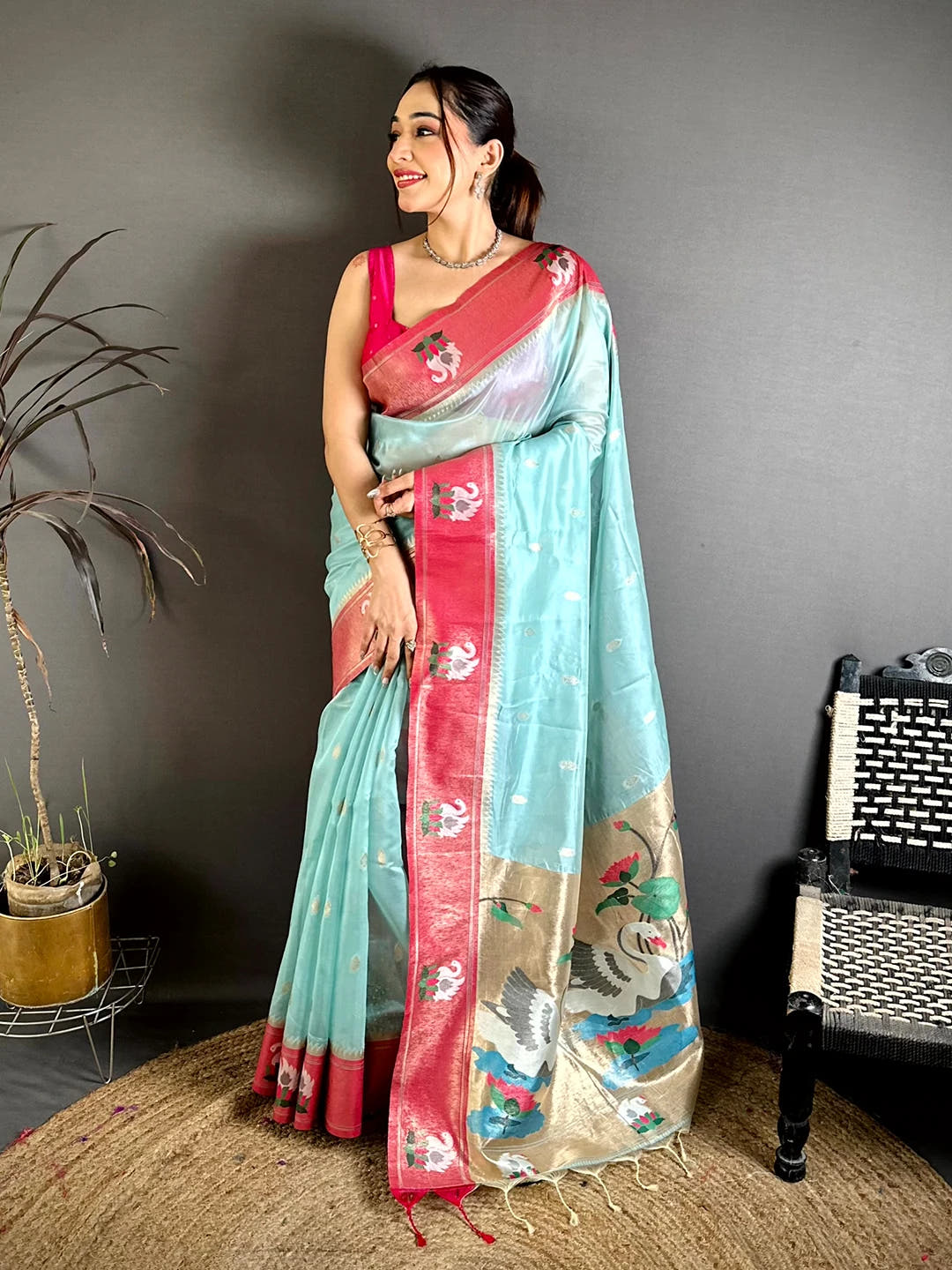 Aqua organza tissue Paithani-style minakari saree, full-length model on jute rug showing rose-pink border and tassels