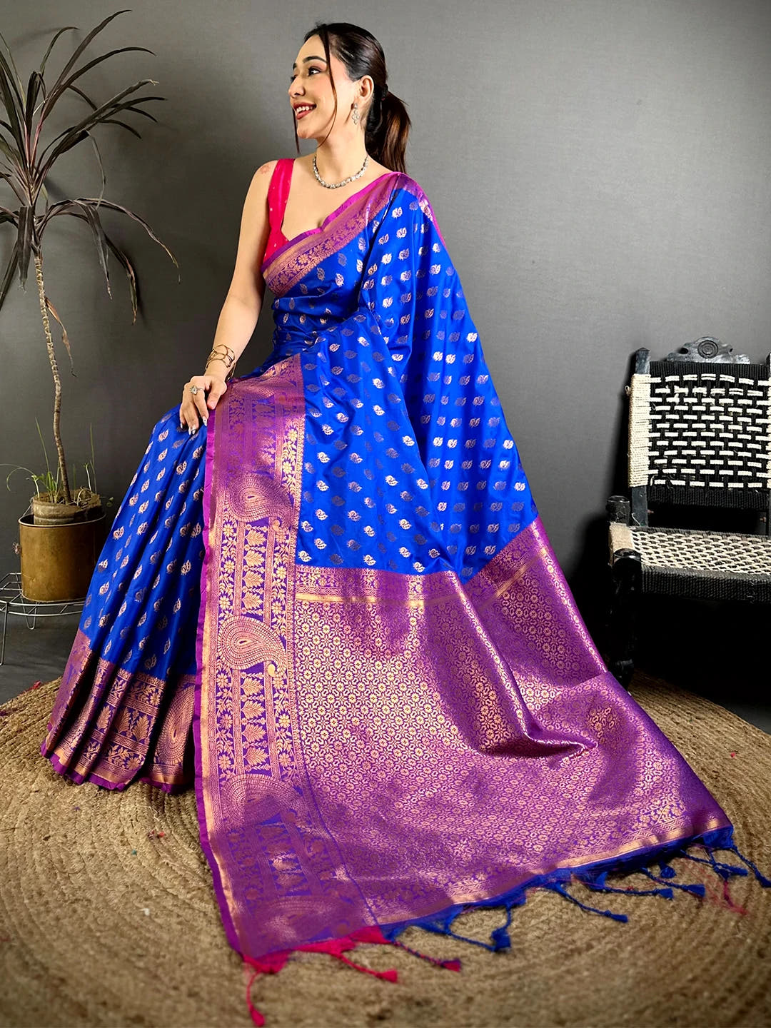 Royal blue soft silk zari woven buta saree, model seated on jute rug with the zari pallu spread out in front