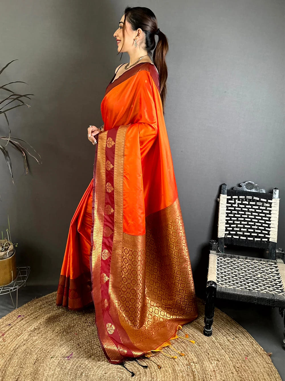 orange silk kanchi-style saree, side view of the model showing the maroon border and the pallu with gold tassels