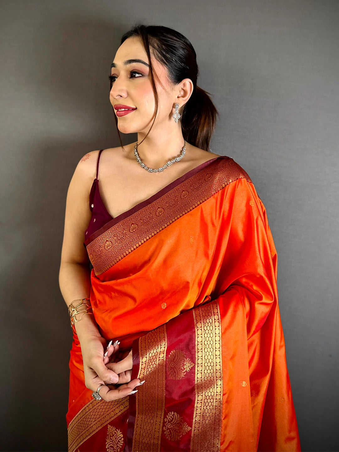 orange silk kanchi-style saree, close-up of the gold zari pallu and maroon border draped over the model's shoulder