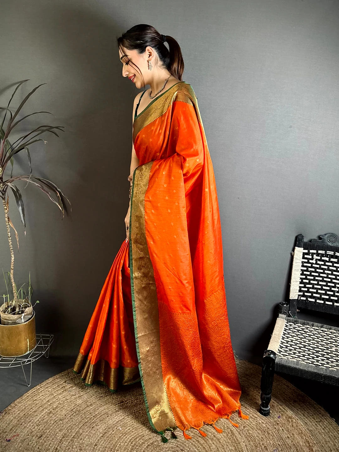 Royal orange raw silk woven buti saree, side view of model with green blouse piece and pleated drape over the shoulder