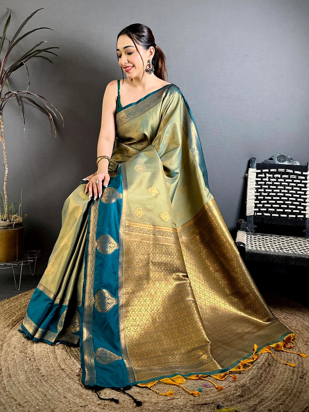 Sage green tissue zari saree, seated pose showing buti motifs, teal paan border and pallu tassels