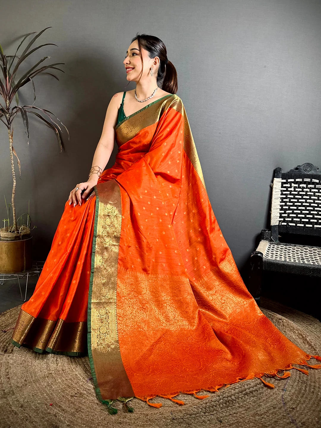 Royal orange raw silk woven buti saree, seated model showing the woven pallu and tassels at the end