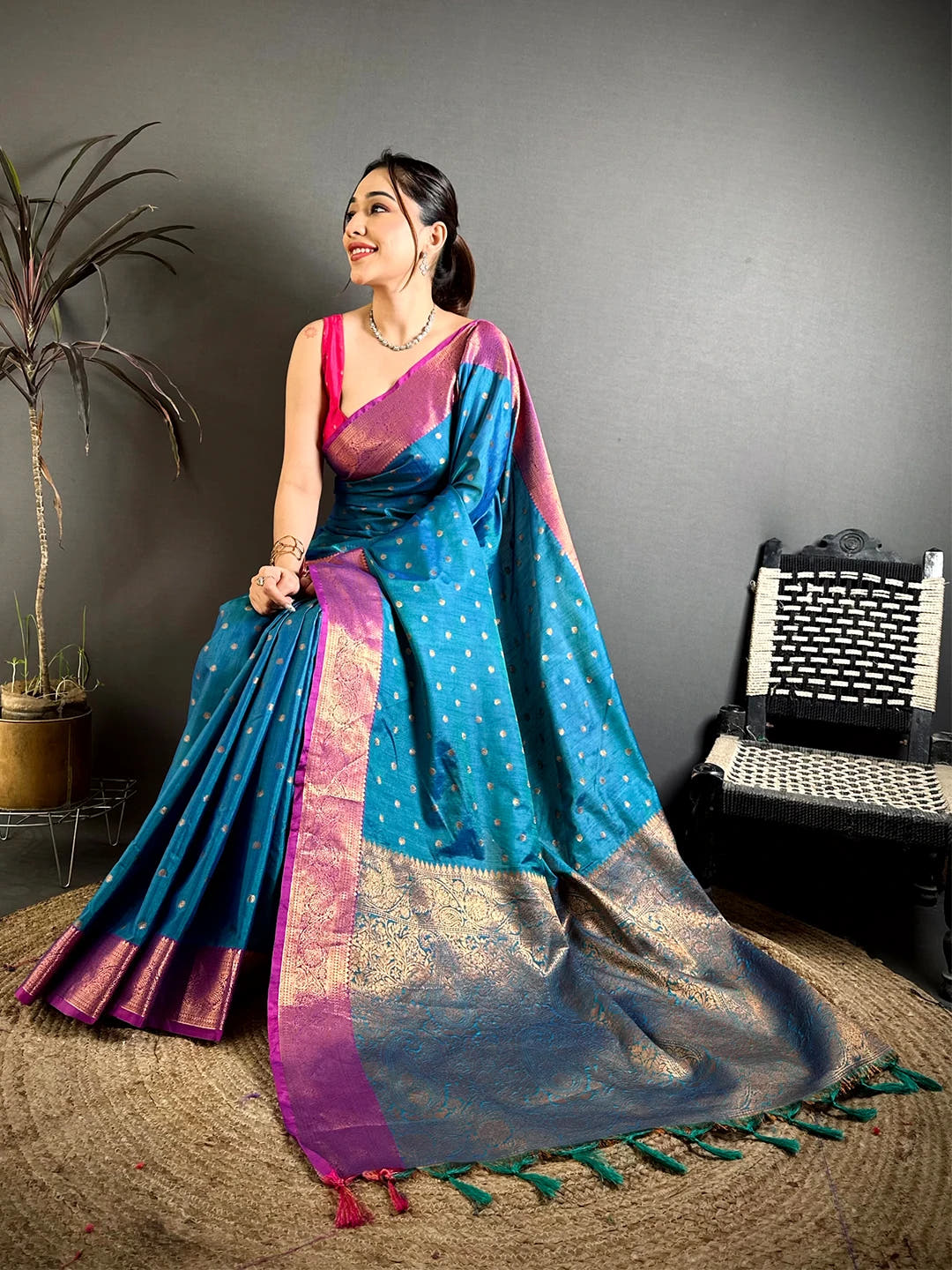 Royal Teal Raw Silk Woven Buti Saree, seated pose showing the woven pallu and green tassel ends on a jute mat